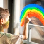 A kid with autism draws rainbow with paint on a window