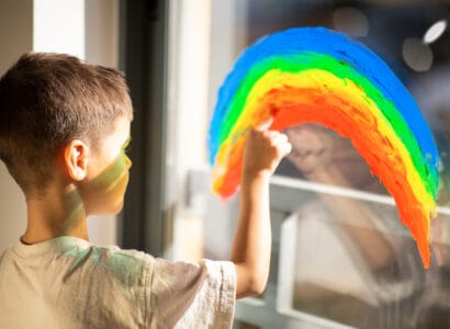 A kid with autism draws rainbow with paint on a window