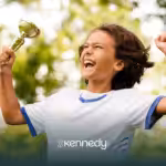 A kid holding a trophy while happily jumping