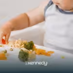 A child eating a variety of vegetables on a high chair