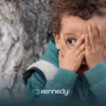A child with autism standing by a tree covering his face with his hands