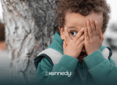 A child with autism standing by a tree covering his face with his hands