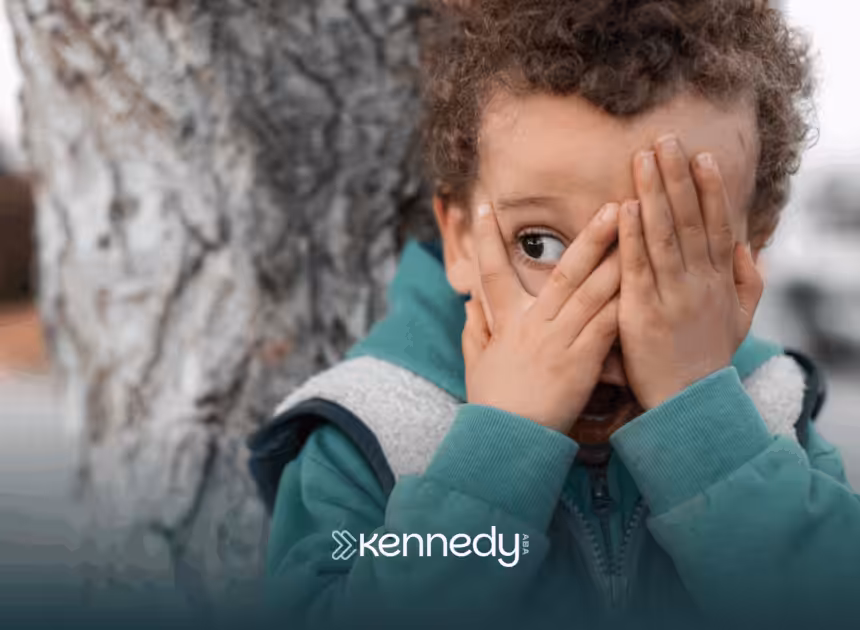 A child with autism standing by a tree covering his face with his hands