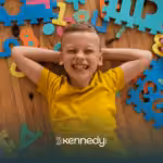 A kid with autism lying on the floor with colorful mat puzzles around him