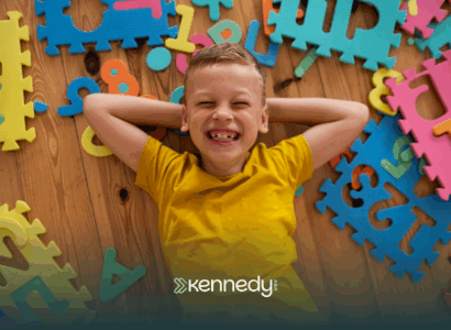 A kid with autism lying on the floor with colorful mat puzzles around him