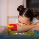 A girl with autism resting her head on the table, looking at colorful building blocks