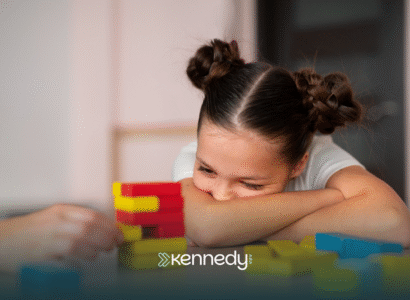 A girl with autism resting her head on the table, looking at colorful building blocks