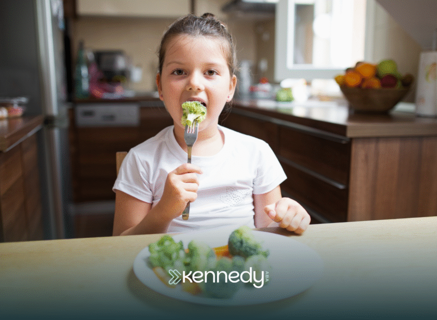 A girl with autism sitting at a table, eating a piece of broccoli