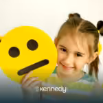 A little girls smiling while holding an emoji paper cutout