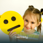 A little girls smiling while holding an emoji paper cutout