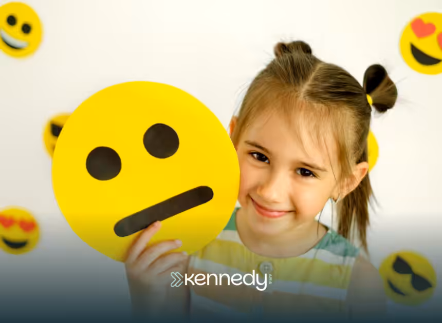 A little girls smiling while holding an emoji paper cutout