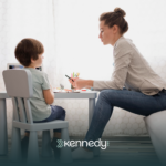 A kid with autism and his ABA therapist sitting at a table while talking during ABA therapy