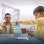 A kid playing with building blocks on a table while his RBT is observing