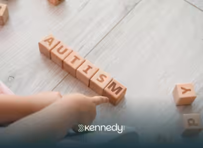 A toddler sitting on a floor, pointing at wooden blocks that spells the word 'autism'