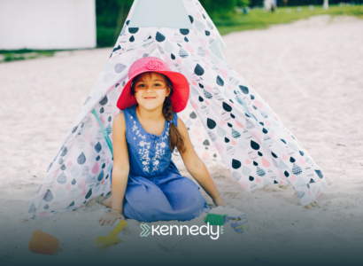 A kid with autism sitting on a sand in front of a tent in a beach