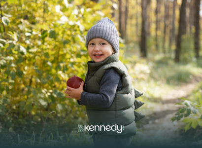 An autistic kid standing outdoors, holding an apple