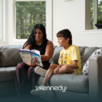 A kid with autism and his ABA therapist reading a book together on a couch during ABA therapy