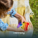 A kid with autism lying on grass, playing with a colorful fidget toy, during summertime