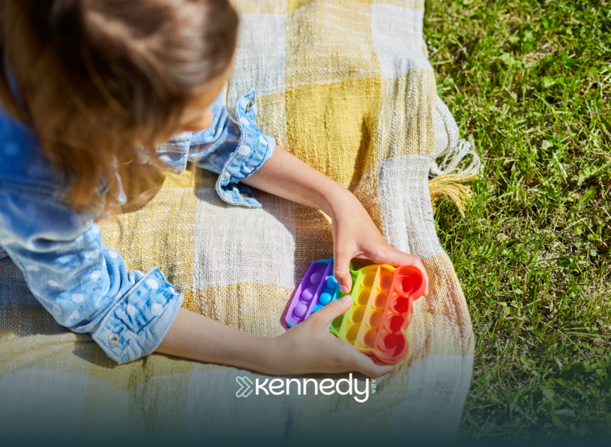 A kid with autism lying on grass, playing with a colorful fidget toy, during summertime