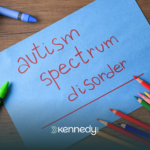 A paper with "autism spectrum disorder" written on it laid out on a wooden table with coloring materials around it