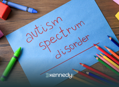 A paper with "autism spectrum disorder" written on it laid out on a wooden table with coloring materials around it