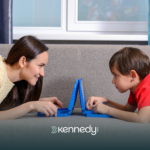 An ABA therapist and a kid with autism using a gadget while laying on a couch during ABA therapy