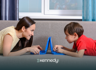 An ABA therapist and a kid with autism using a gadget while laying on a couch during ABA therapy