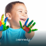 A kid with autism happily showing his hands covered in colorful hand paint