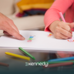 A kid drawing on a paper using coloring pencils with an evaluator guiding her