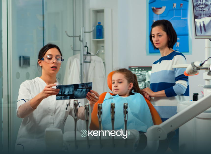 A kid with autism sitting on a dental chair during a dental checkup with her mother behind her