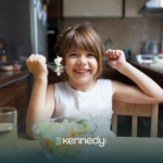 A kid happily eating vegetables on a table